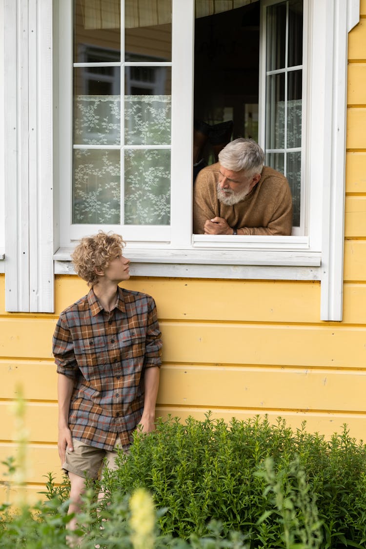 Teenager Standing Near Wall And Grandfather Leaning Out Of Window