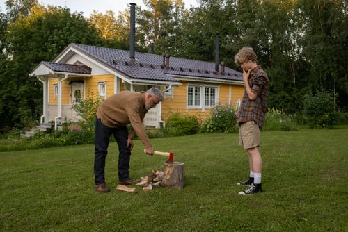 Free Grandfather teaching grandson to chop wood in a backyard setting. Scenic summer day. Stock Photo