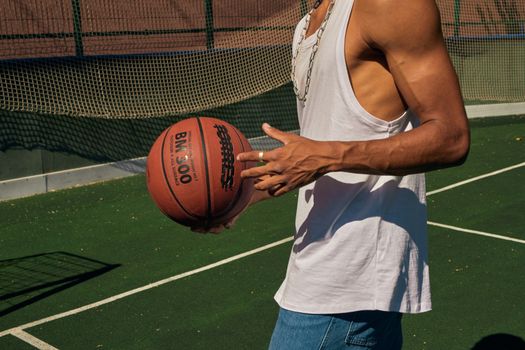 Close-up of a man holding a basketball on an outdoor court, wearing a sleeveless shirt.