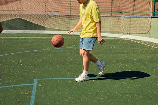 Adult male casually dribbling a basketball on a sunny outdoor sports court.