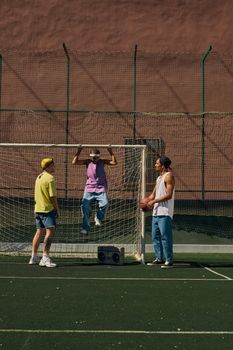 Three teenagers enjoying a sunny day at an outdoor sports court with a basketball and boombox.