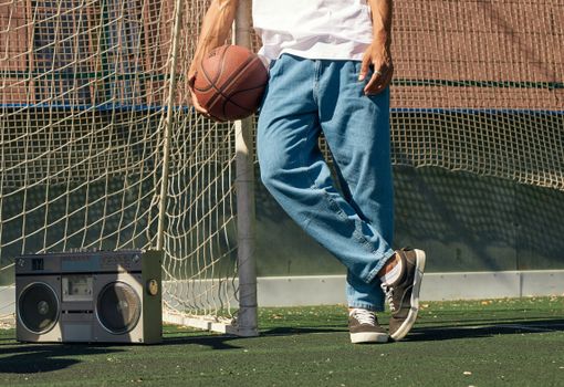 A man in casual attire holding a basketball next to a boombox on an outdoor court.