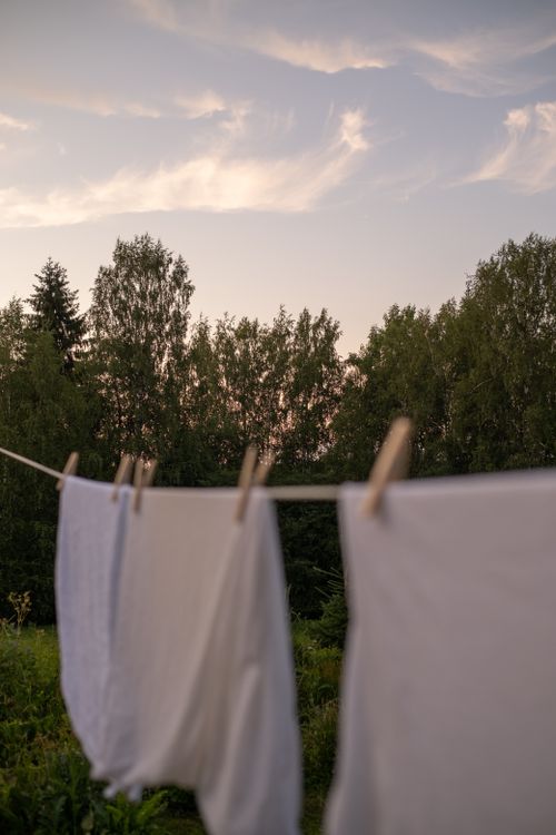 Free White linens drying on a clothesline in a serene outdoor setting at sunset. Stock Photo