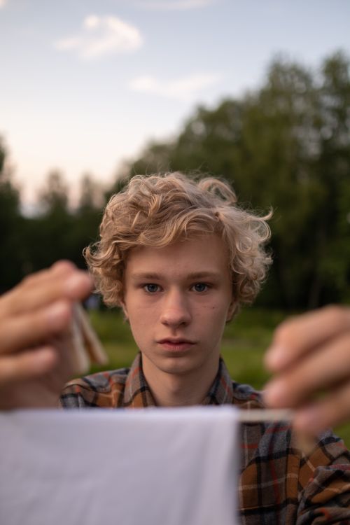Free Teenage boy with curly blond hair hanging white cloth outdoors. Perfect for casual lifestyle themes. Stock Photo