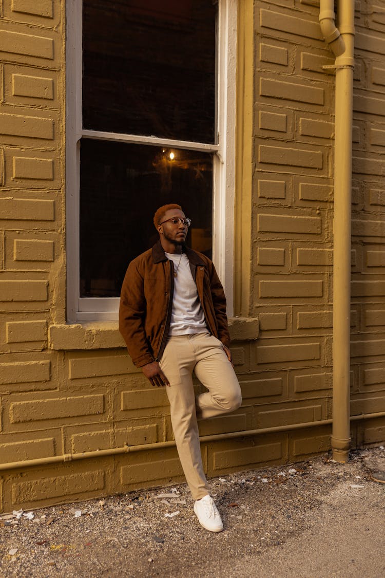 Man Wearing Glasses Leaning Against Wall Of Building