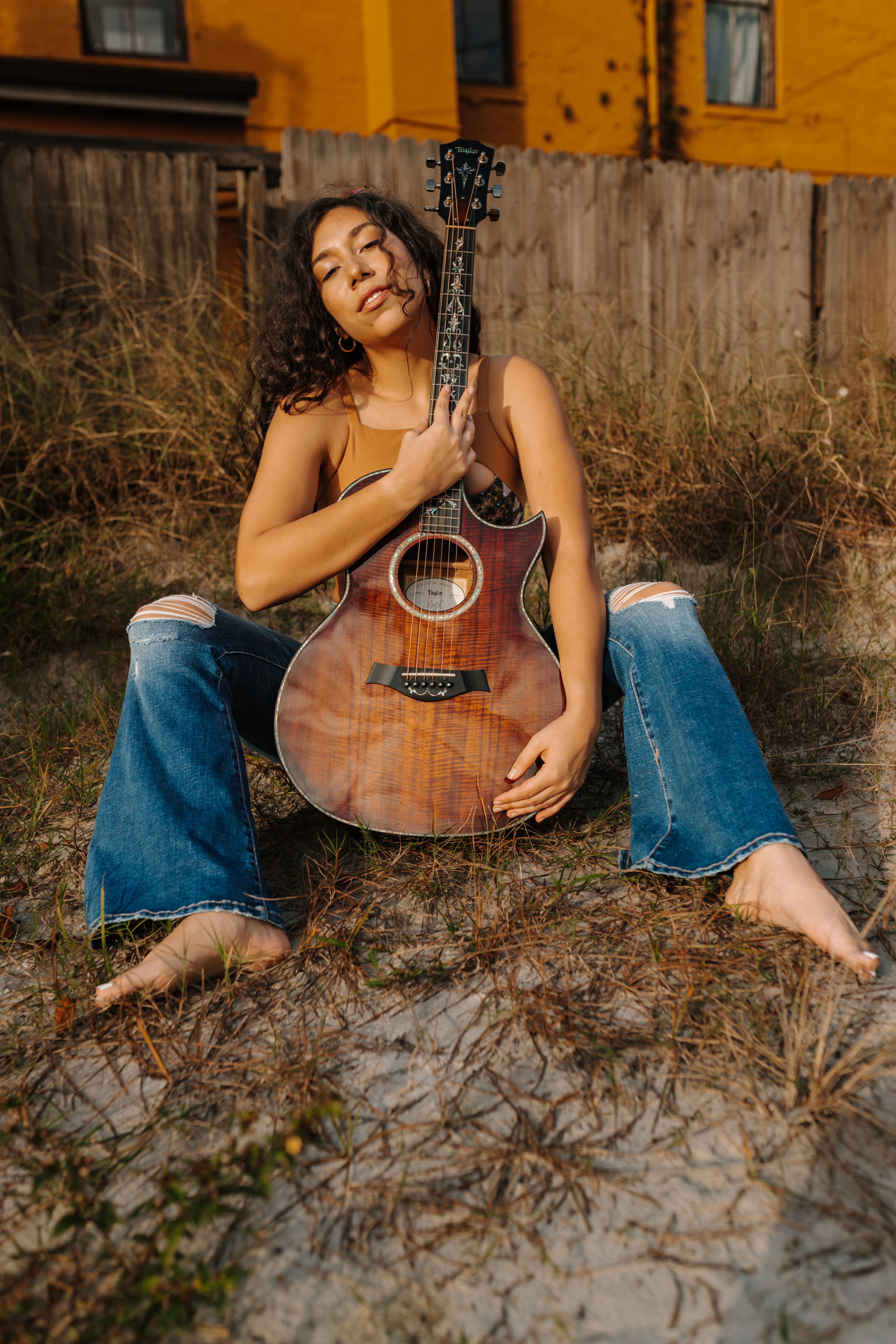 Woman sitting outdoors with an acoustic guitar, enjoying a sunny day.