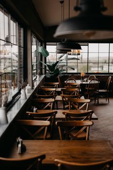 Warm restaurant setting with wooden tables and chairs, potted plants, and large windows.