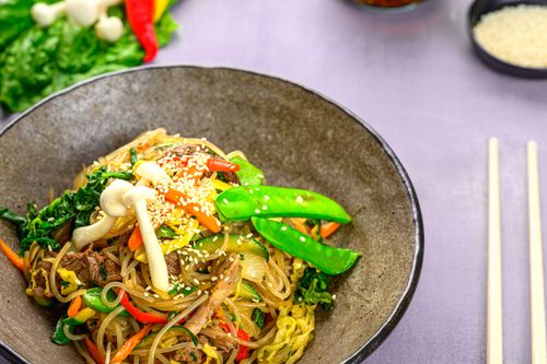 Free A vibrant bowl of Asian stir-fry with colorful vegetables, mushrooms, and sesame seeds served with chopsticks. Stock Photo