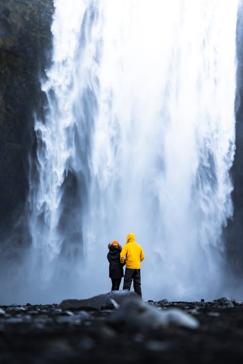 Free Couple Standing at Foot of Waterfall and Holding Hands Stock Photo