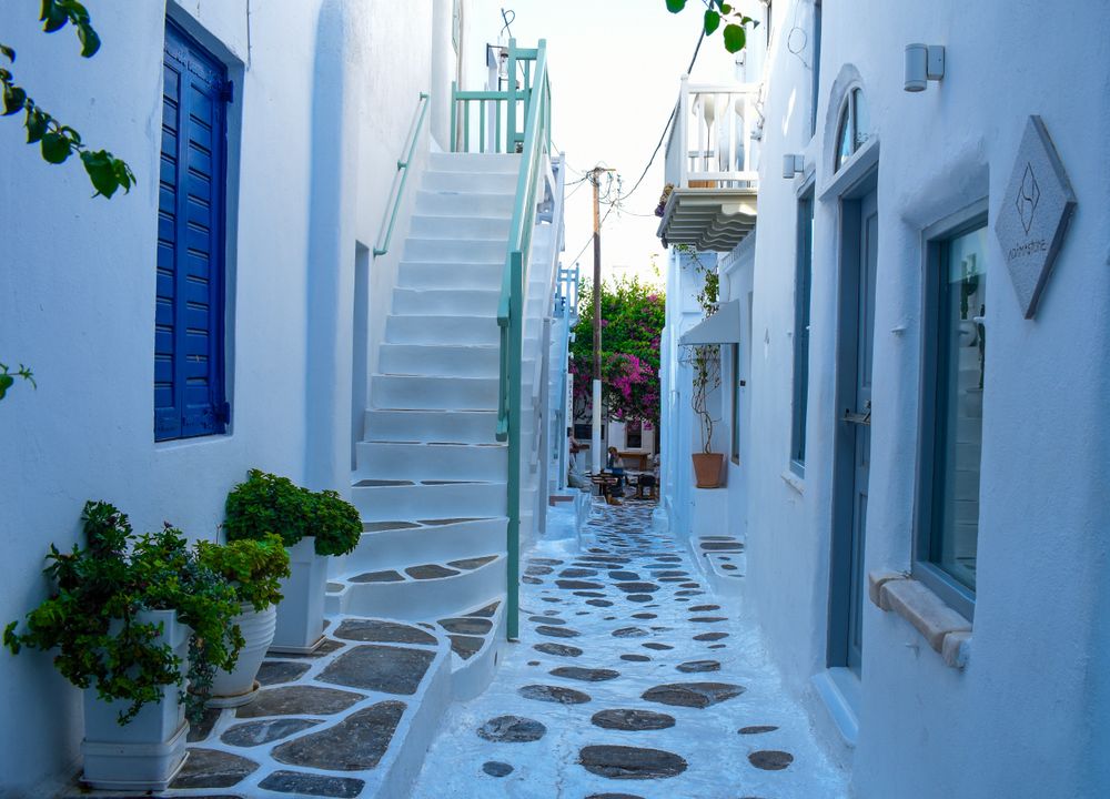 Callejón cíclada con casas de persianas azules, escaleras y suelo empedrado