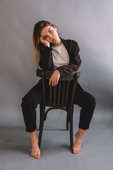 Young woman posing barefoot on a chair in a studio with a thoughtful expression.