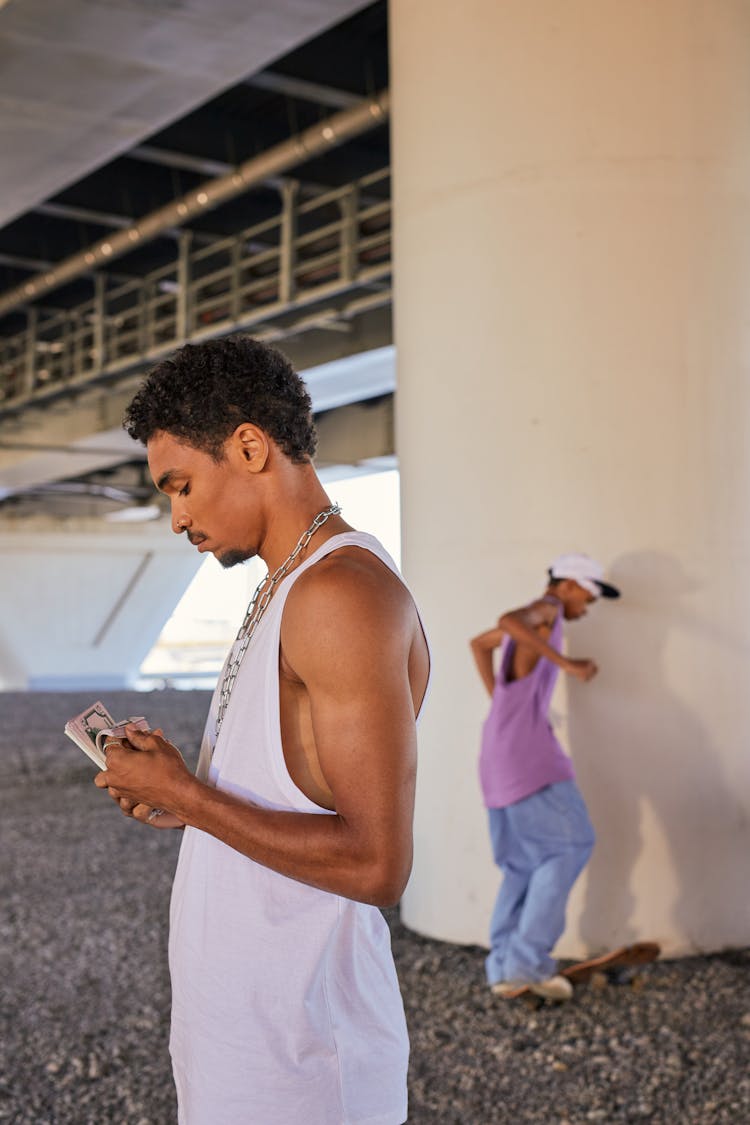 A Man In A White Tank Top Counting Cash