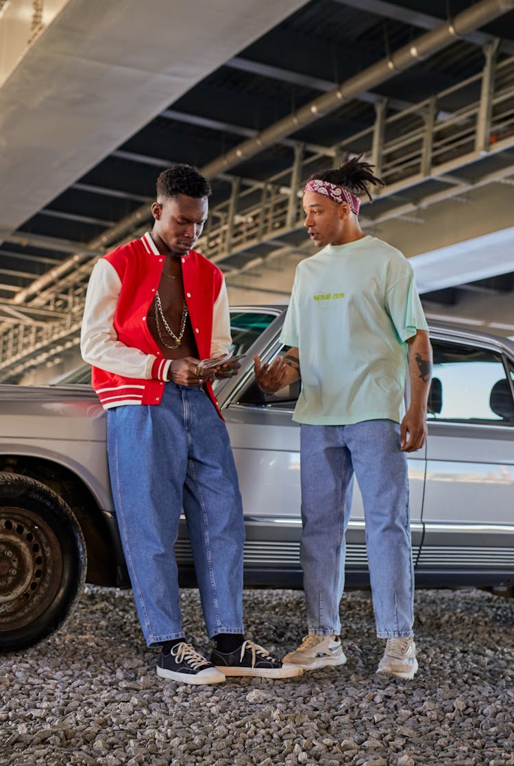 A Person Talking To A Man Counting Cash While Leaning On A Car