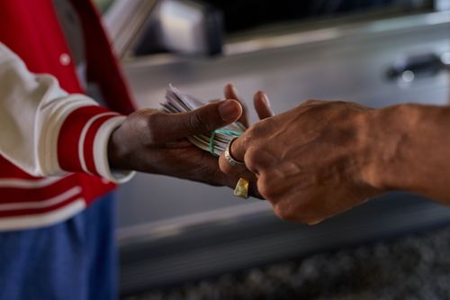 Free A detailed shot of two hands exchanging a bundle of cash outside by a car. Stock Photo