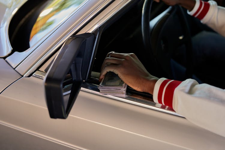 A Person Holding Cash While Driving A Car