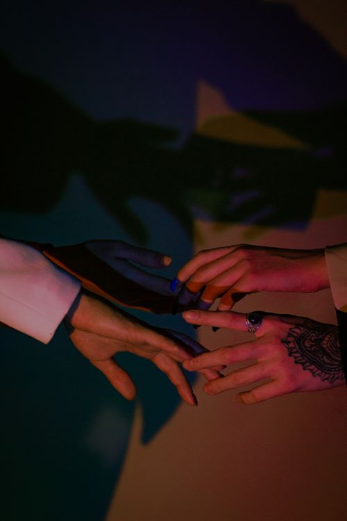 Free Dramatic close-up of hands reaching towards each other, creating captivating shadows with colorful lighting. Stock Photo