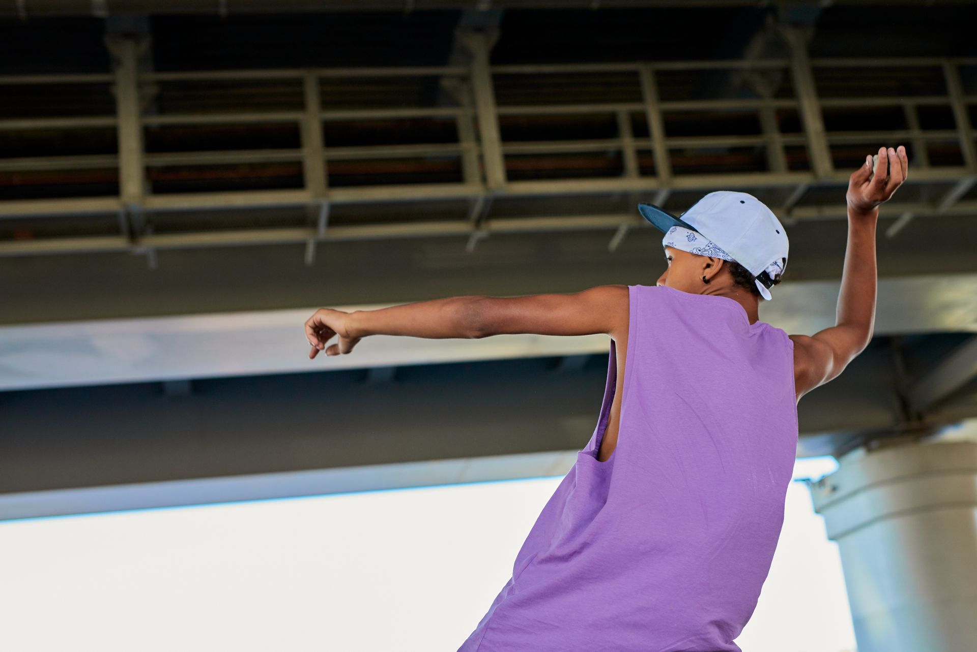 Young man in a purple shirt dancing energetically under a city bridge.