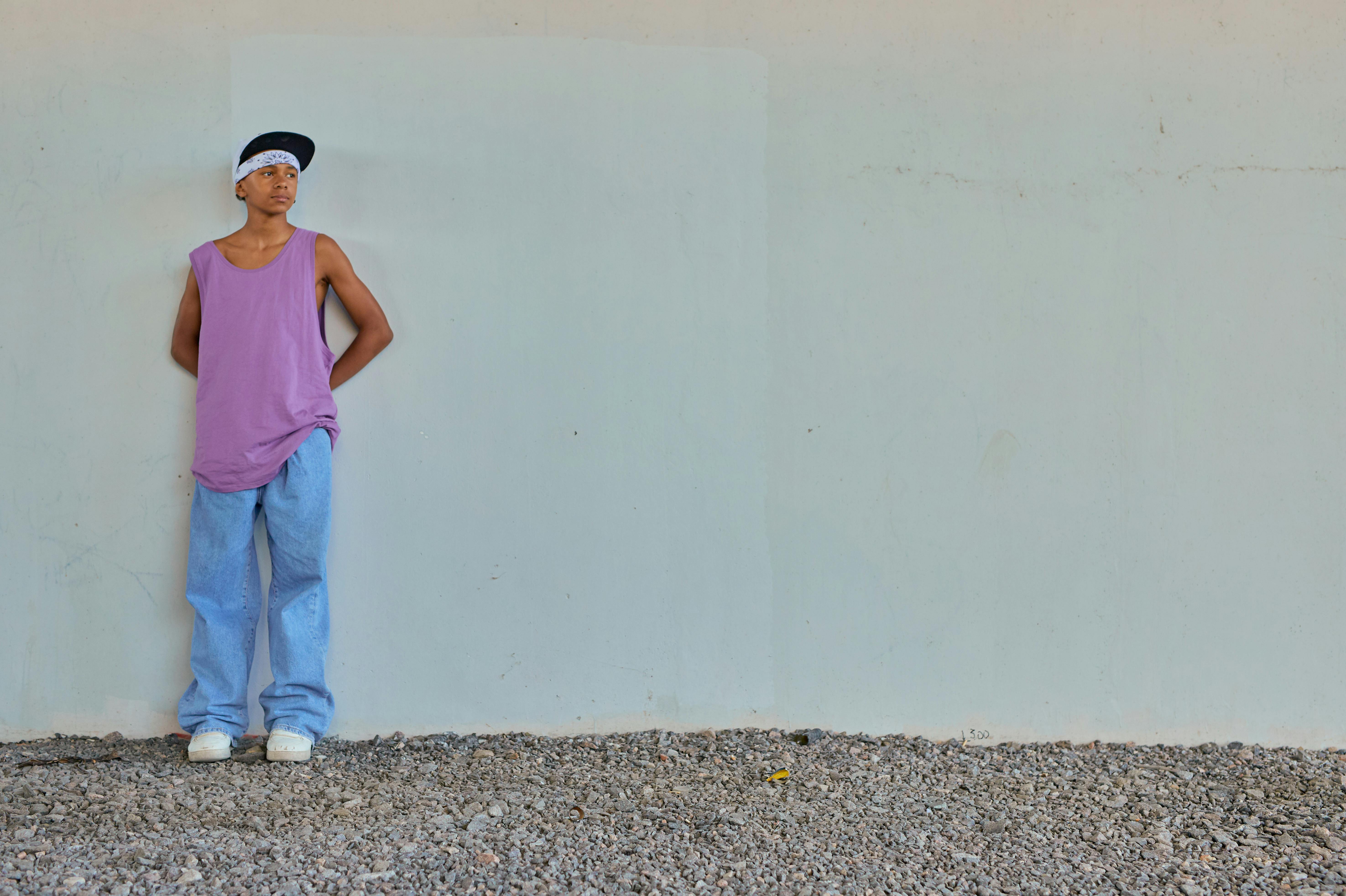 man in pink tank top and blue denim jeans standing beside white wall