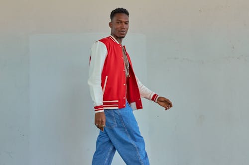 Free Man Wearing Red and White Jacket Walking Beside White Wall Stock Photo