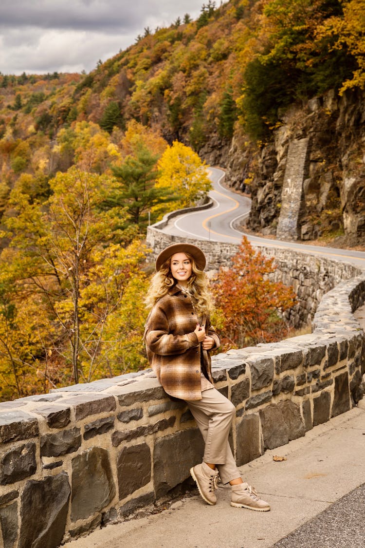 Woman In Brown Jacket Sitting On A Road Barrier