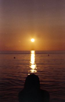 Silhouette of a person against a warm Sicilian sunset over the calm sea, creating a serene evening scene.