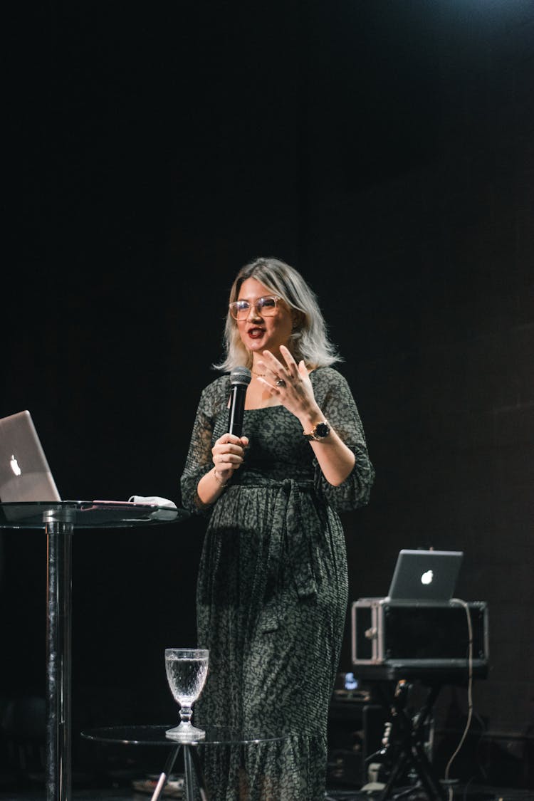 A Woman Talking On The Microphone While On Stage