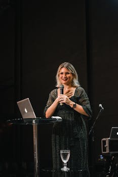 A woman giving a presentation on stage with a microphone and laptop.