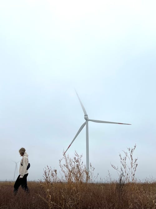 Person Walking near Wind Turbine under Clouds