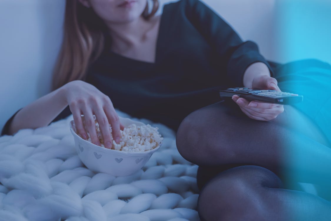 Free Woman in White Bed Holding Remote Control While Eating Popcorn Stock Photo