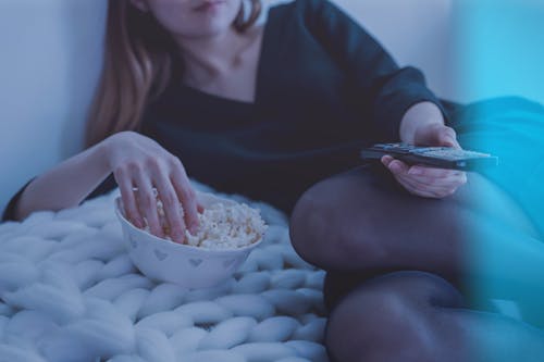 Mujer En La Cama Blanca Sosteniendo El Control Remoto Mientras Come Palomitas De Maíz