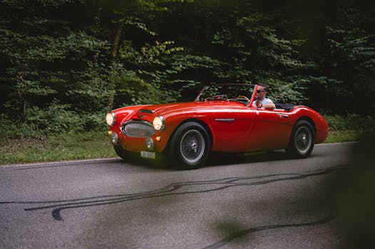 A vibrant red vintage convertible car driving along a forest road, capturing timeless travel elegance.