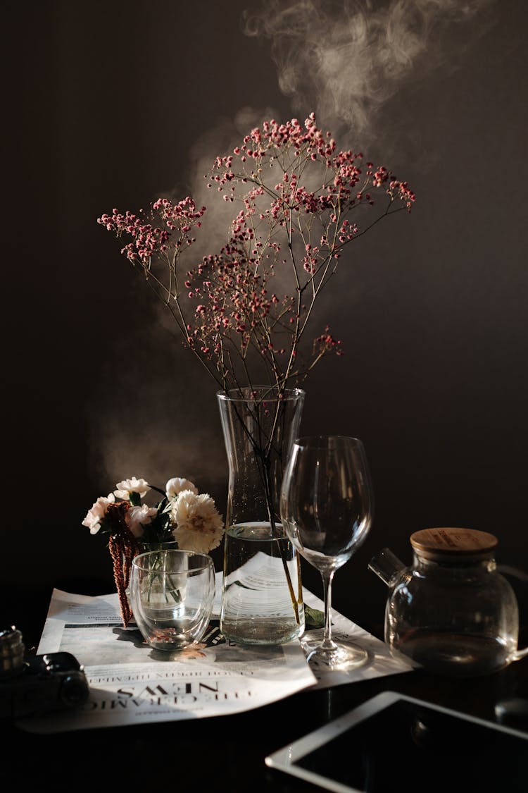 Glass Utensils And Cut Flowers In Artistic Arrangement With Smoke In Background