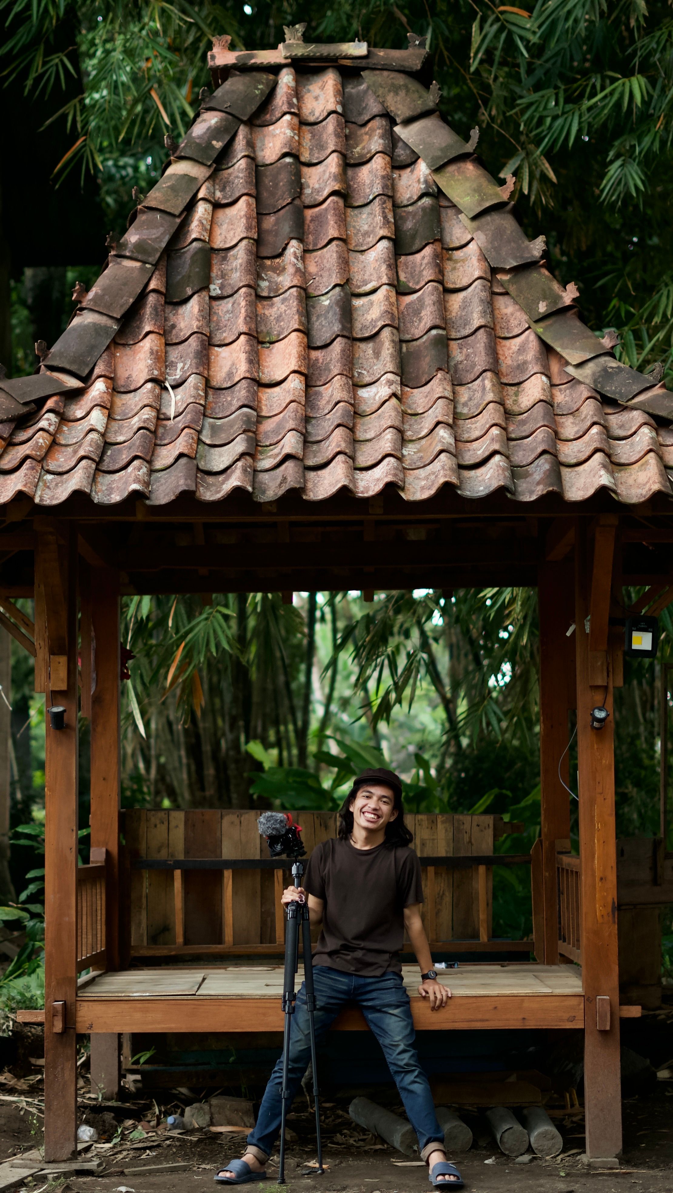 Photographer sitting with tripod in a Central Java hut, smiling.