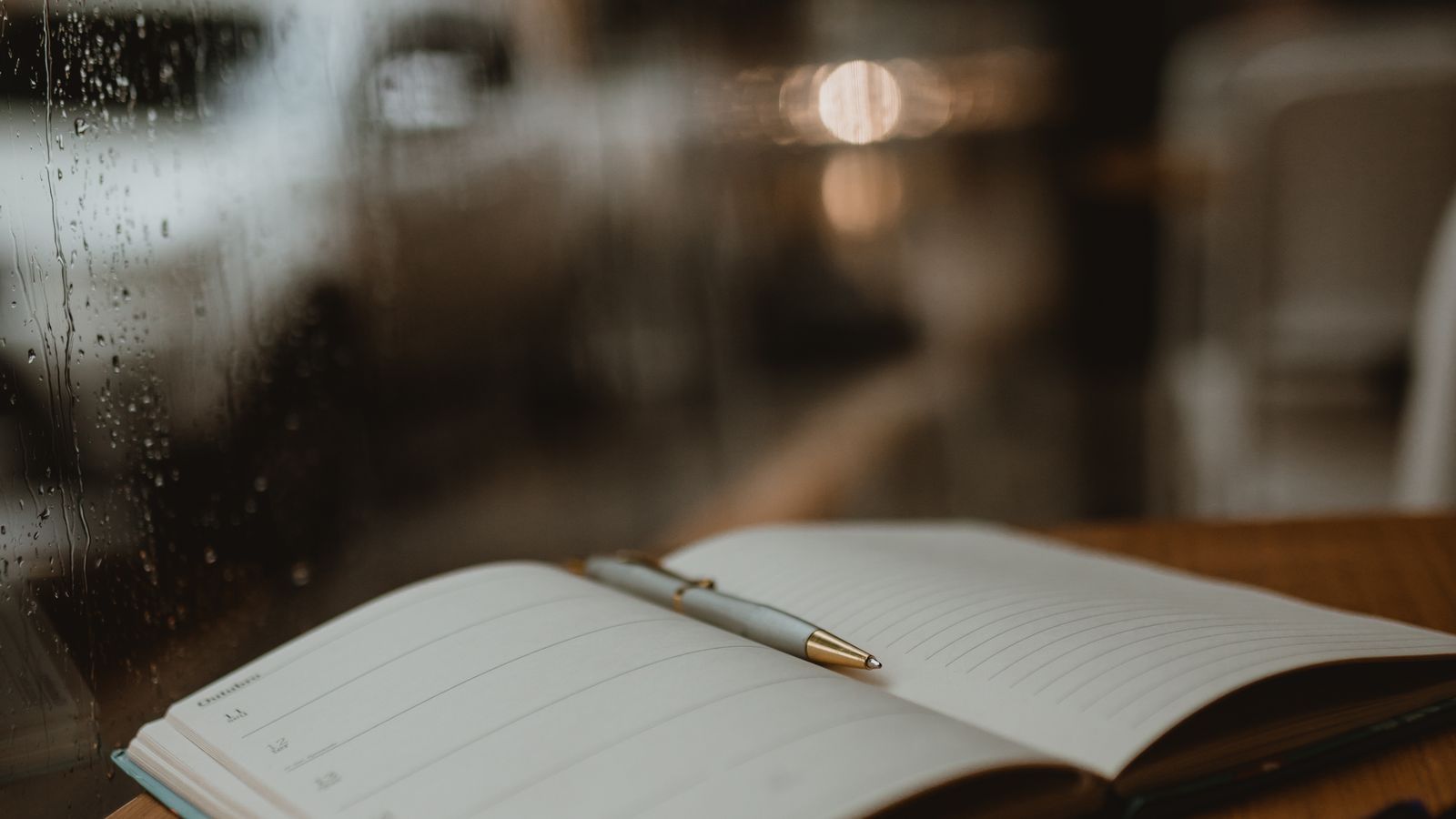 An open notebook and pen beside a rain-covered window
