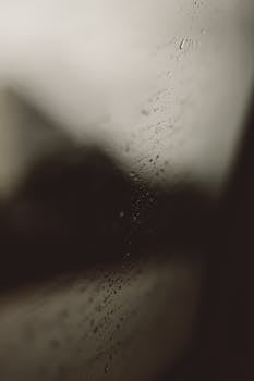 A close-up view of raindrops trickling down a glass window, creating a moody atmosphere.