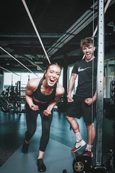 Two friends laughing and flexing muscles during a gym workout, embodying a healthy lifestyle.
