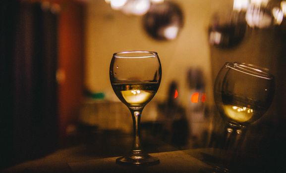 A close-up of a white wine glass with a blurred, warm-toned background in a cozy setting.