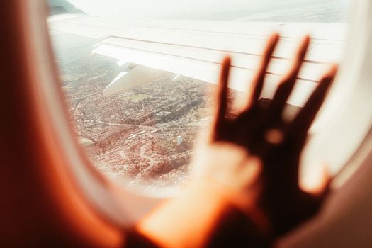 A scenic view from an airplane window with a hand silhouette against the cityscape below.