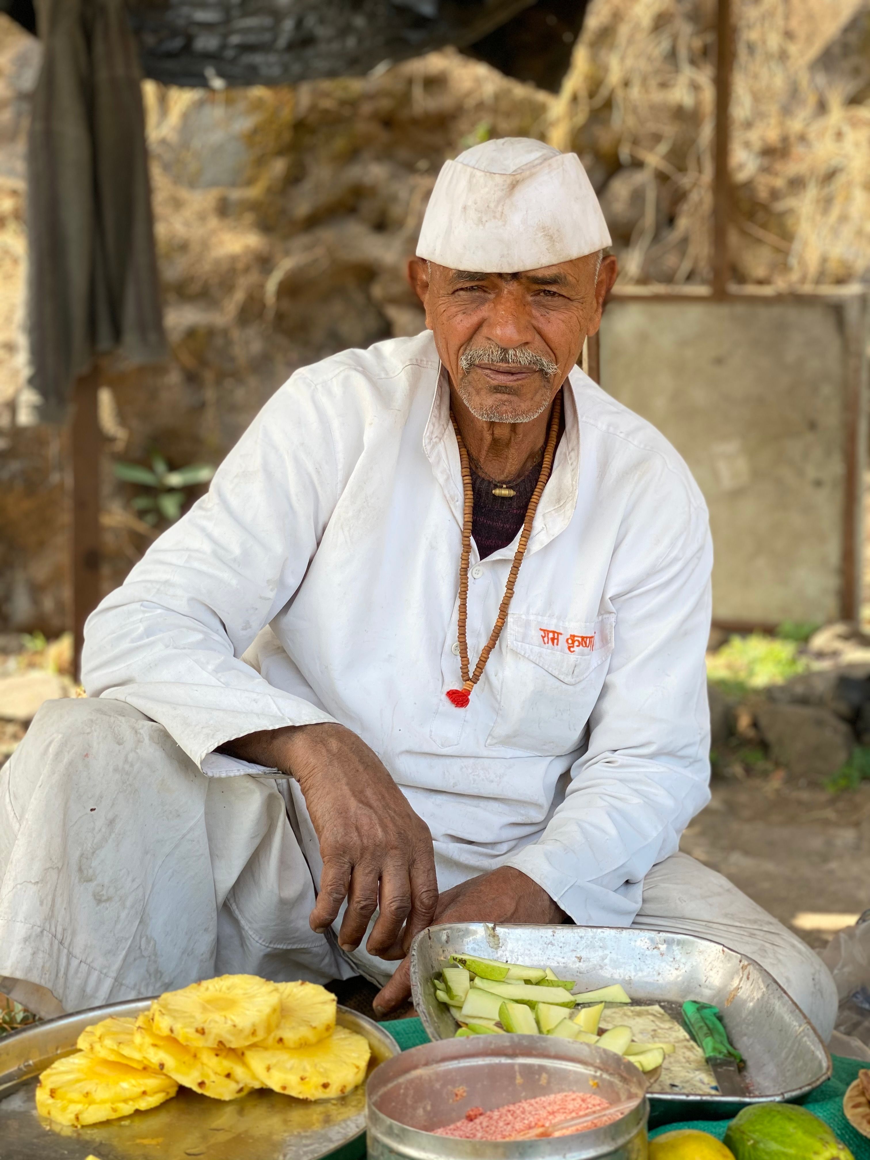 Elderly vendor in traditional attire selling fresh pineapple slices on a street in India.