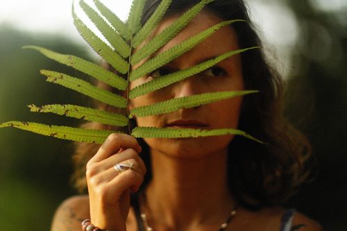 Free Close-up of a woman holding a fern leaf, partially covering her face outdoors. Stock Photo