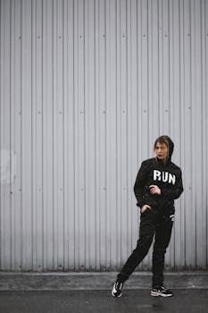 一个穿着黑色运动服的人正对着户外的灰色墙壁摆姿势，准备行动