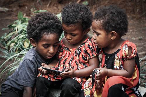 Free Three children using a smartphone outdoors in Papua New Guinea, exploring technology together. Stock Photo