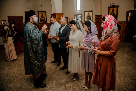 A religious wedding ceremony with priest and couples in a church, holding candles.