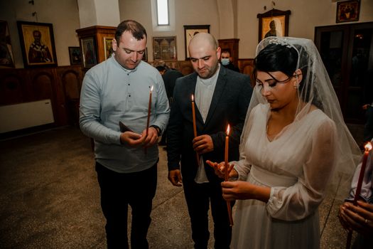 Bride and guests holding candles during an Orthodox wedding ceremony in a church setting.