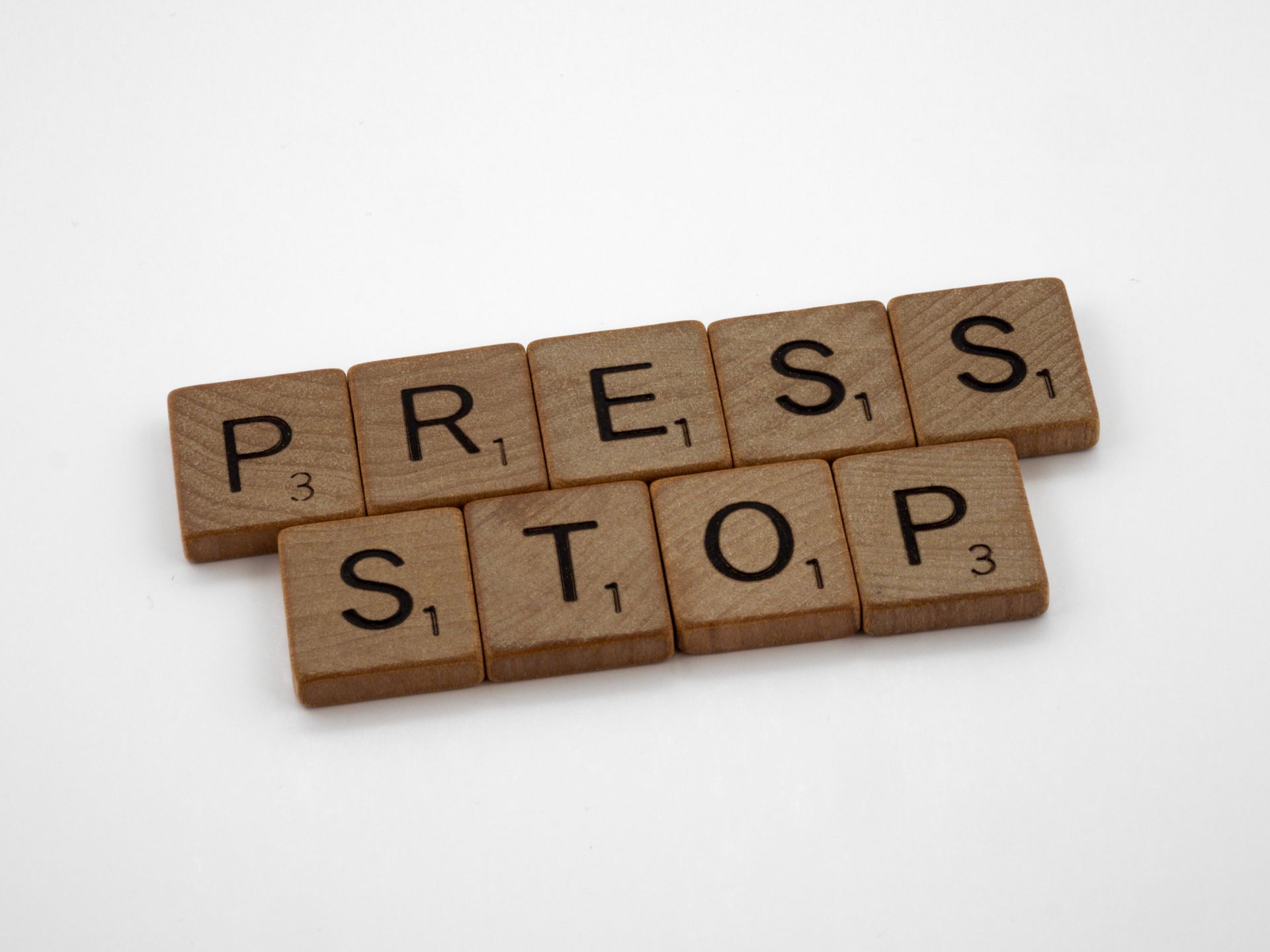 Wooden Scrabble tiles forming the words 'Press Stop' on a white surface.