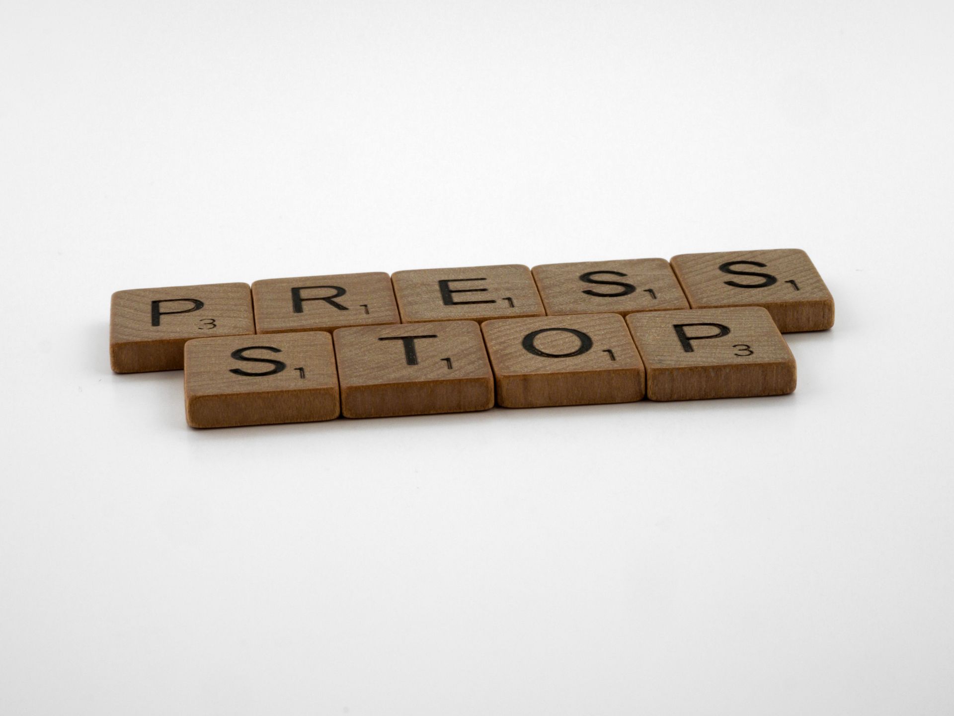 Close-up of wooden Scrabble tiles forming the words 'Press Stop' on a white surface.