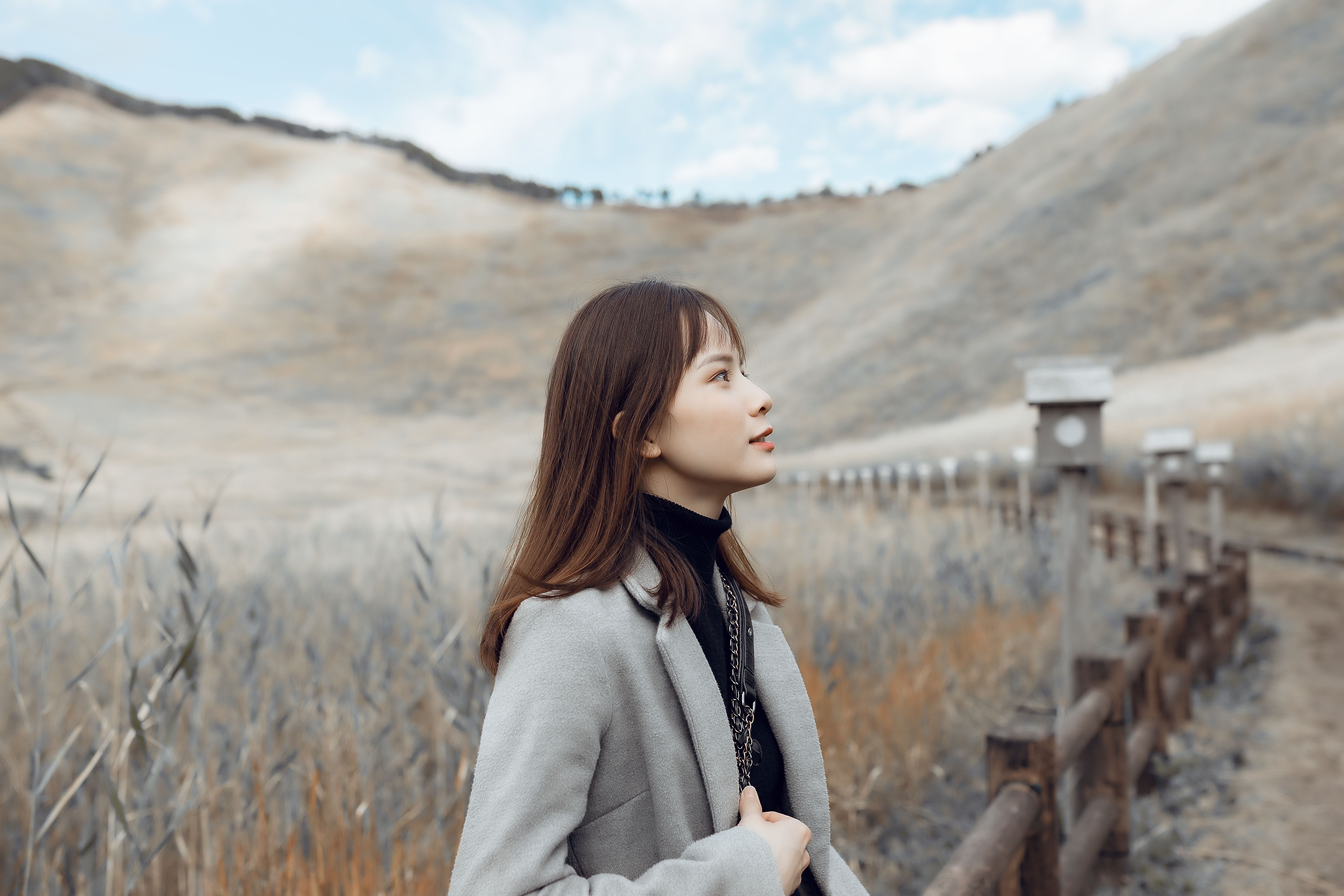 Asian woman in a serene mountain landscape, looking thoughtful and composed.
