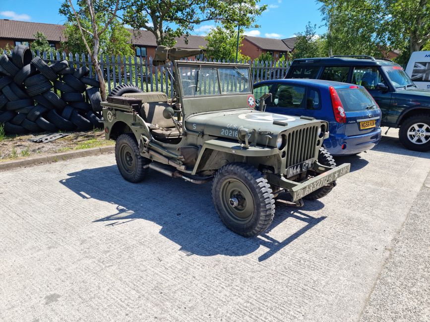 A vintage Willys MB jeep parked outdoors in Burscough, England, on a sunny day.