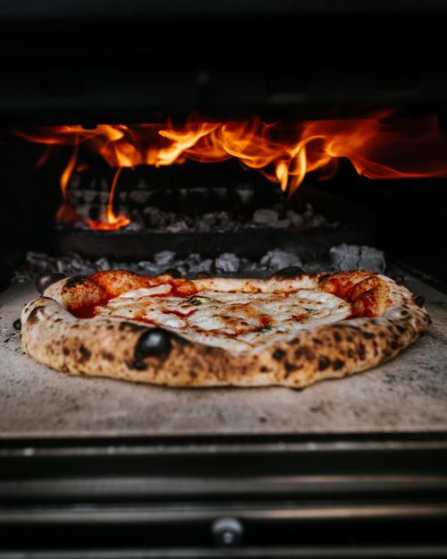 Free Close-up of authentic pizza cooking in a wood-fired oven with flames. Stock Photo