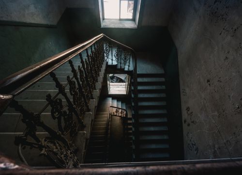 Free Eerie view of an abandoned building's interior stairs with dim lighting and a vintage handrail. Stock Photo